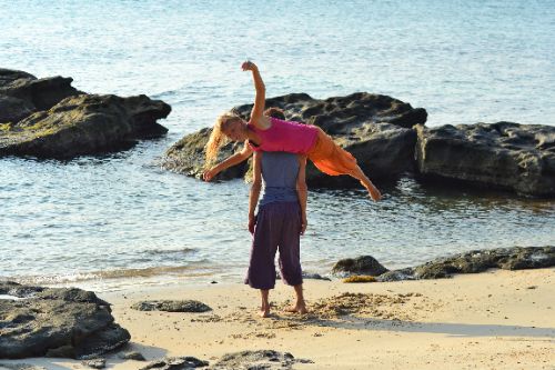 Elinmaria and gabriel dancing contact improvisation on a beach with rocks and sea as background