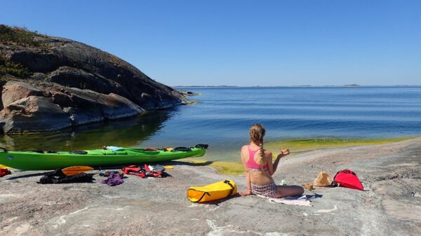 A girl enjoying a tea in the sea shore by her kayak