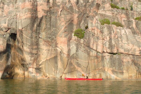A person and a red kayak in front of a huge stone wall