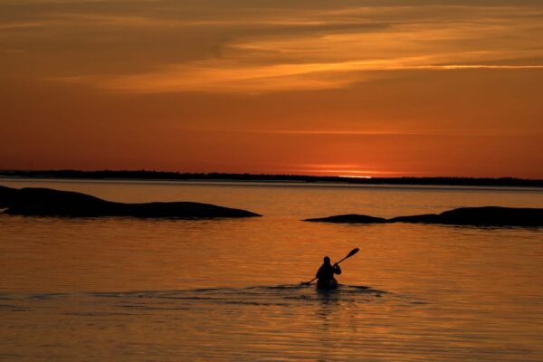 Henkilö meloo kohti oranssia auringonlaskua saaristomerellä