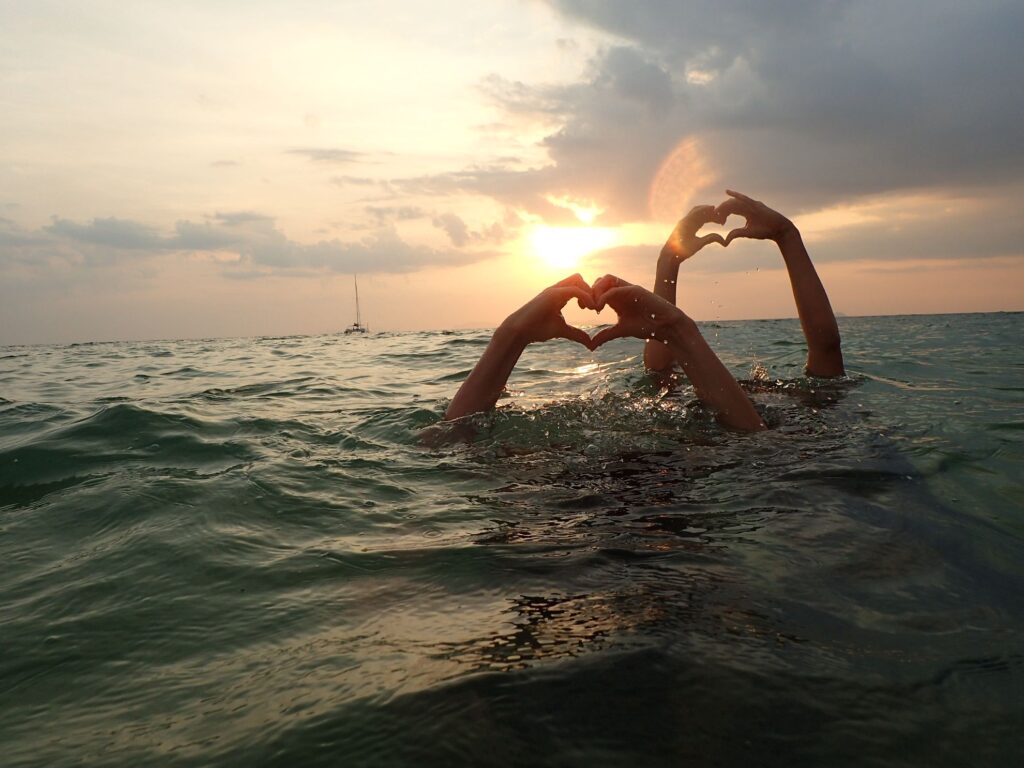 Two hands with heart shape emerging from the surface of the water