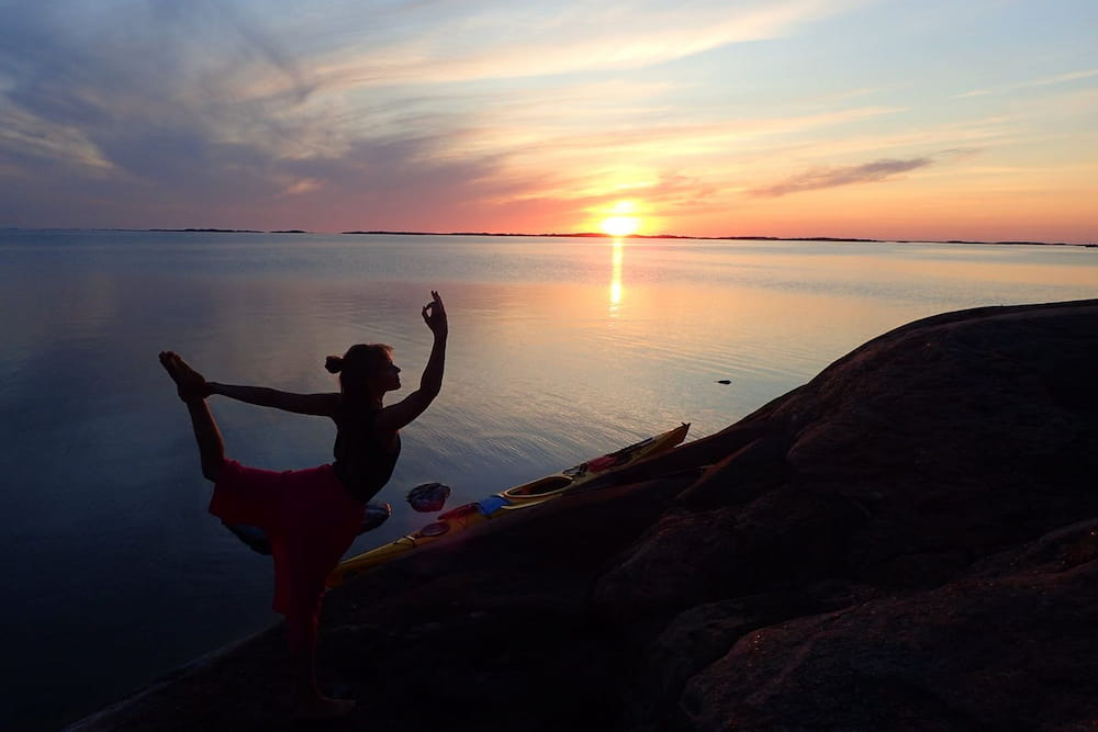 Siluetten av ElinmMaria som gör yoga i solnedgången på Skärgårdshavet.