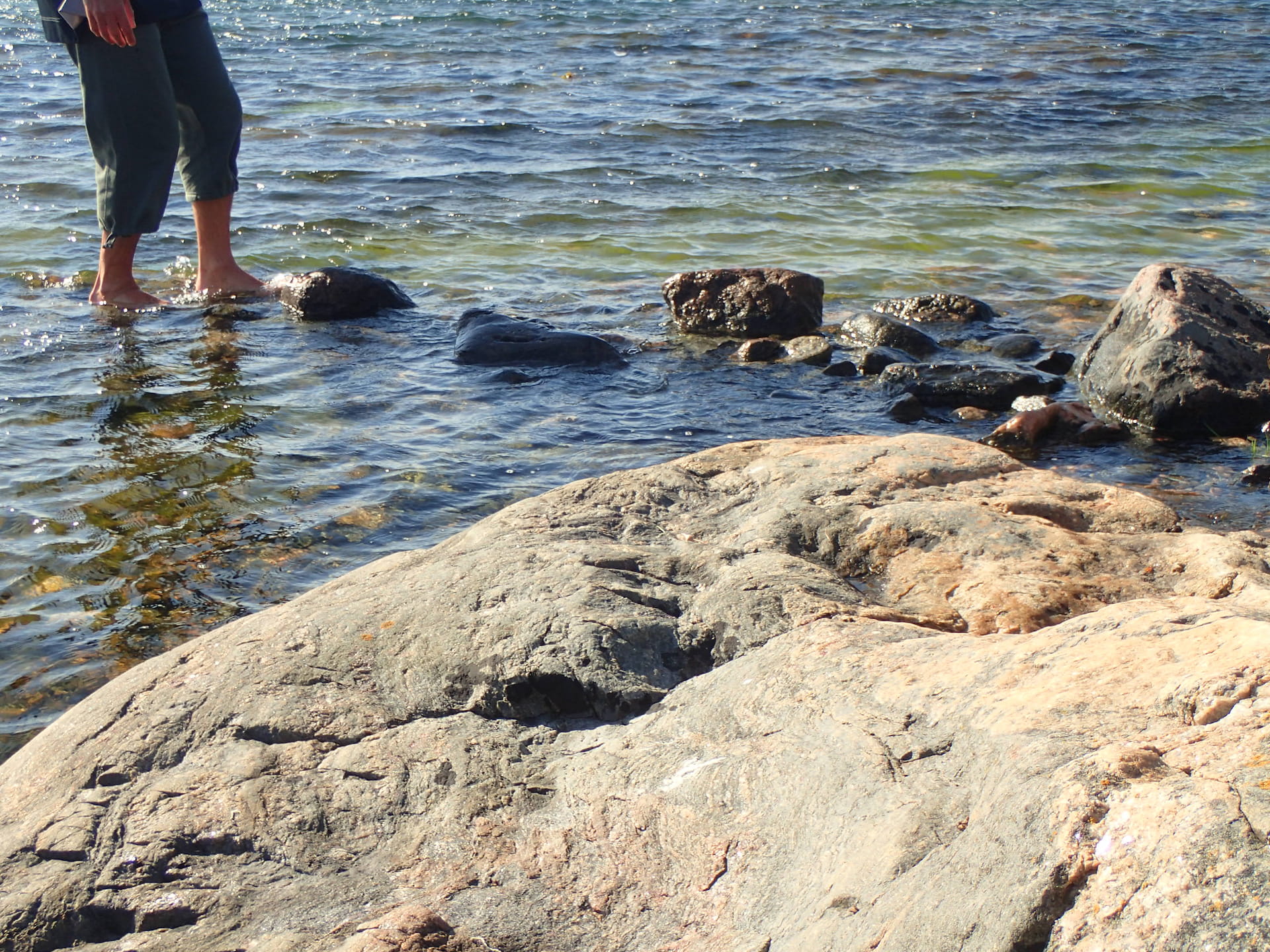 A person standing with his feet in the water by the rocks