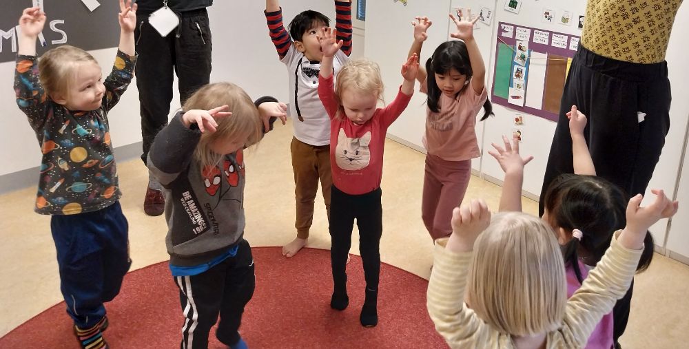 A group of kindergarten children dancing with their arms raised.