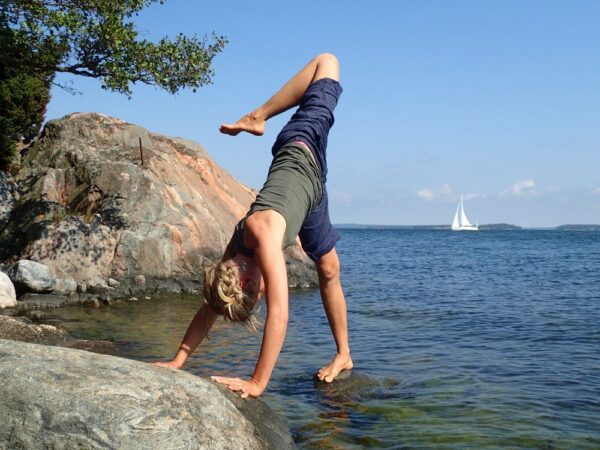 ElinMaria in a yoga pose on the seawater with a sailboat in the background