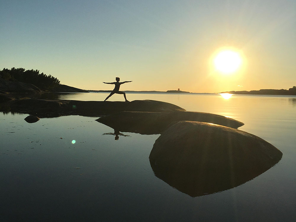 Siluetten av ElinmMaria som gör yoga i solnedgången på Skärgårdshavet.